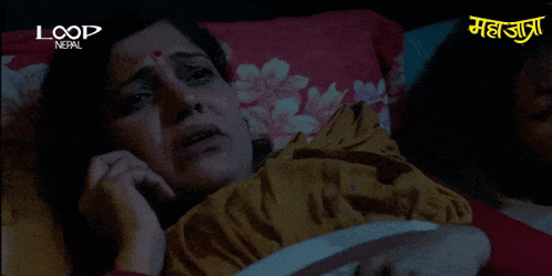 a woman laying in bed talking on a cell phone with loop nepal in the corner