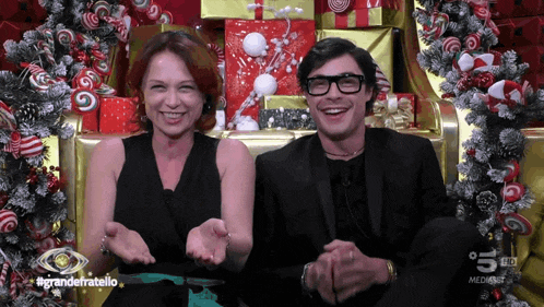 a man and a woman are sitting next to each other in front of a christmas tree with the words grandefratello on the bottom