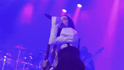a woman singing into a microphone in front of a purple light