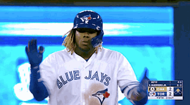 a man in a blue jays jersey is standing in front of a scoreboard