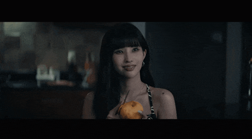 a woman with long black hair is holding an orange and looking at the camera