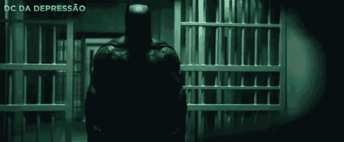 a man in a batman costume is standing in a jail cell behind bars .