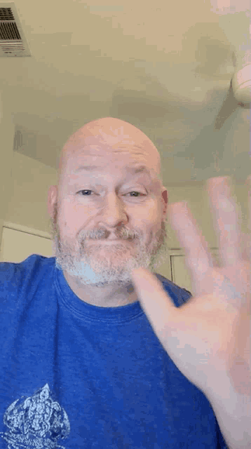 a bald man with a beard wearing a blue shirt is waving