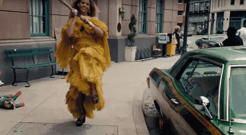 a woman in a yellow dress is running down a street with a green car behind her .