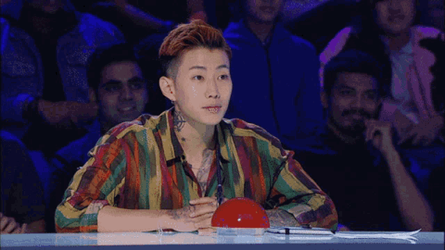 a man with a tattoo on his arm sits at a table in front of a red button that says ' sd '