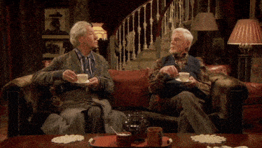 two older men sit on a couch holding cups of tea with the words i 'm visible in pink