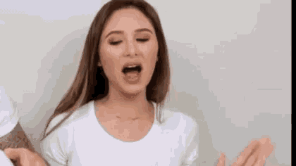 a woman in a white t-shirt is making a funny face with her mouth open and her hands outstretched .