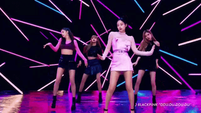 a group of women are dancing together on a stage in front of a neon background .