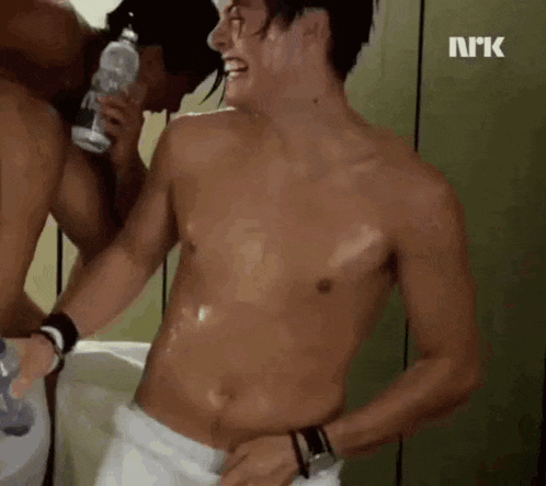 a shirtless man with a towel around his waist is standing next to another shirtless man holding a bottle of water .