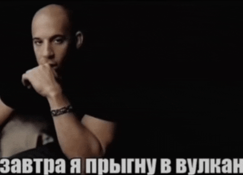 a bald man with a bracelet on his wrist is sitting in a dark room with a caption in russian