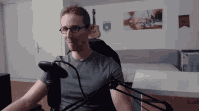 a man wearing glasses is sitting in front of a microphone in a room
