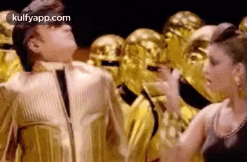 a man and woman are dancing in front of a crowd of gold statues .