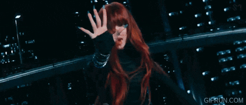 a woman with red hair is waving at the camera while two other women are dancing .