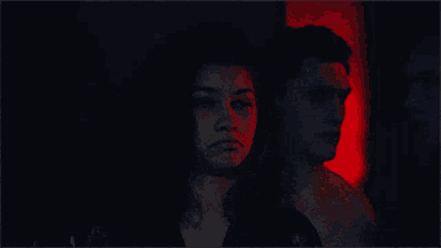 a man and a woman are standing in a dark room with red lights behind them