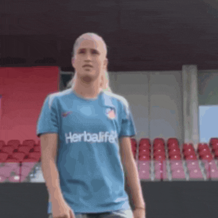 a woman in a blue herbalife shirt is standing in front of a stadium