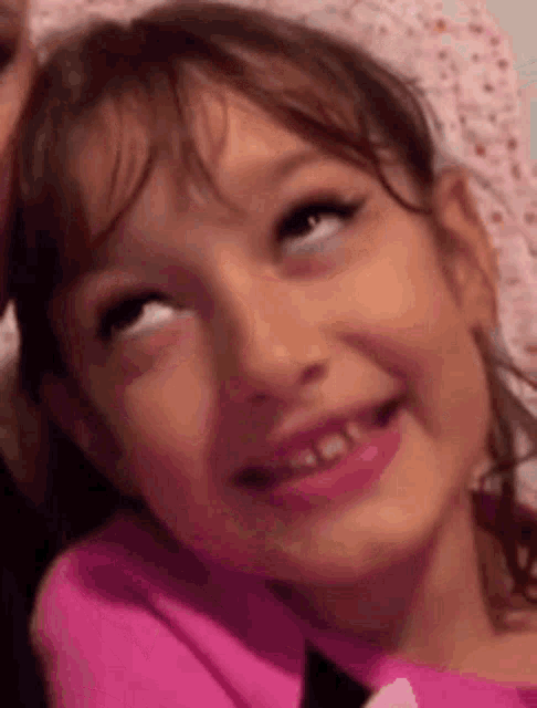 a little girl in a pink shirt is smiling and making a funny face .