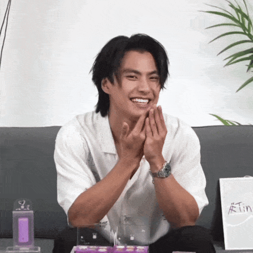 a man in a white shirt is sitting on a couch with his hands folded