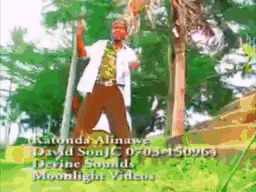 a man in a white shirt and brown pants stands in front of a tree with his arms in the air