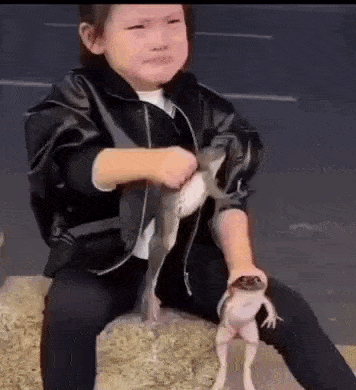 a little girl is sitting on a rock holding a lizard .