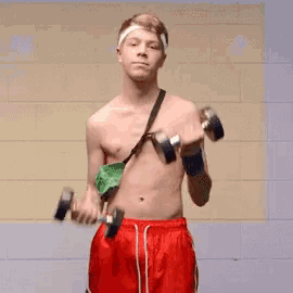 a shirtless man wearing red shorts is lifting dumbbells