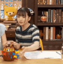a woman sits at a table with a yellow teddy bear on top of her head