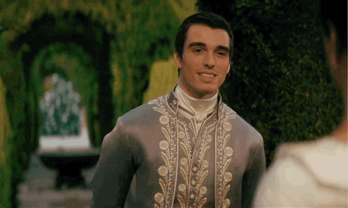a man in a grey and gold embroidered coat smiles