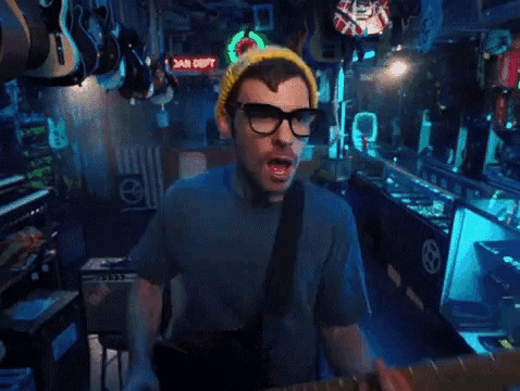a man wearing glasses and a yellow beanie is playing a guitar in a store .
