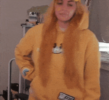 a woman wearing a yellow hoodie with a fragile sticker on the sleeve