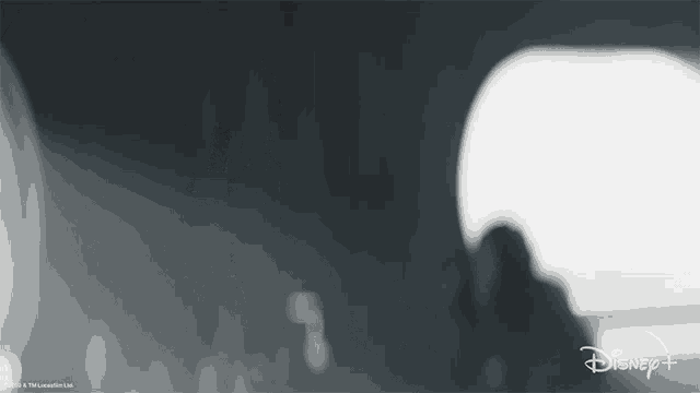 a blurred image of a person in a dark room with a disney + logo in the corner