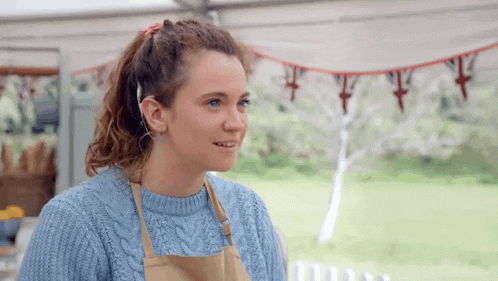 a woman wearing a blue sweater and apron is smiling .