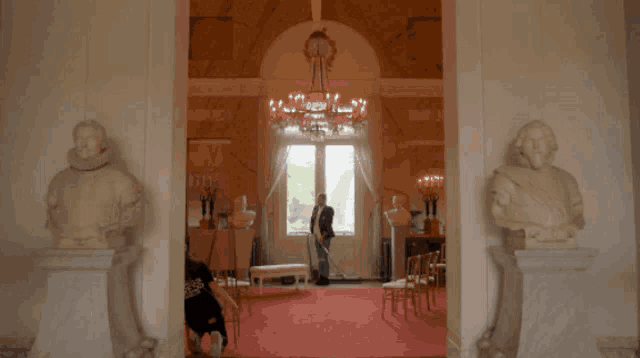 a man in a suit is standing in a room with statues and a chandelier