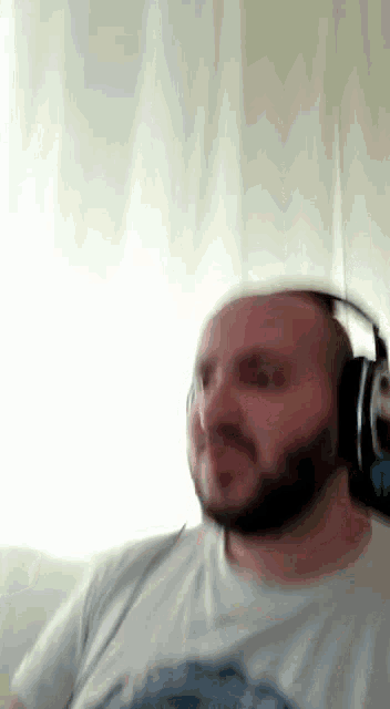 a man with a beard wearing headphones and a white shirt is sitting on a couch .