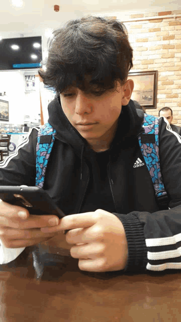 a boy wearing a black adidas jacket looks at his phone