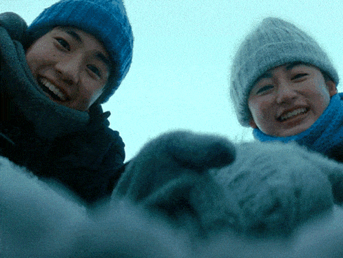 two people wearing knitted hats and scarves are smiling