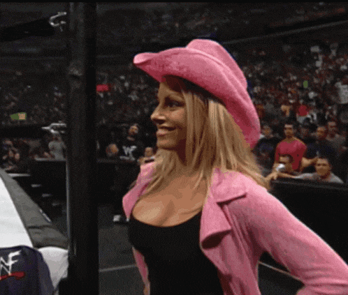 a woman wearing a pink cowboy hat stands in front of a crowd of people