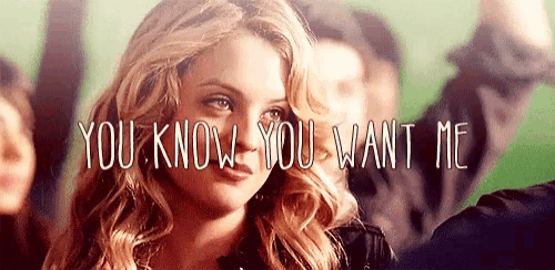 a woman is standing in front of a crowd with the words `` you know you want me '' on her face .