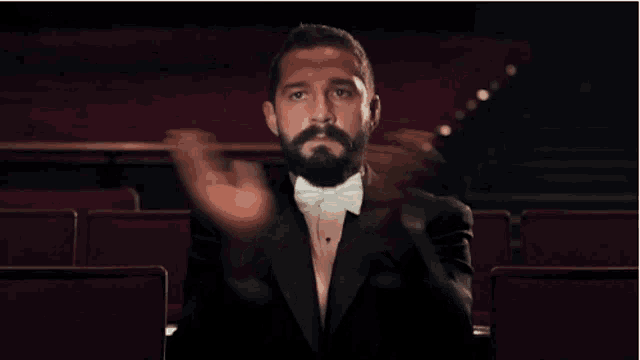 a man in a tuxedo and bow tie is clapping in a theater