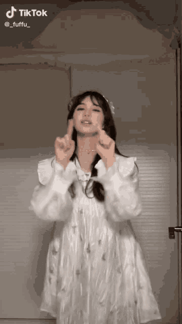 a woman in a white dress making a heart with her hands