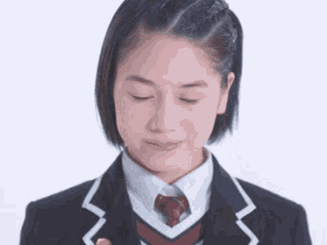 a girl in a school uniform and tie is looking down