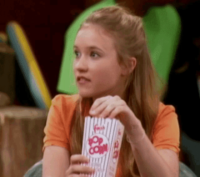 a girl is holding a striped container of popcorn .
