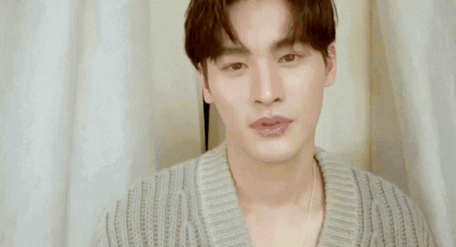 a young man in a tan sweater holds his hand to his head
