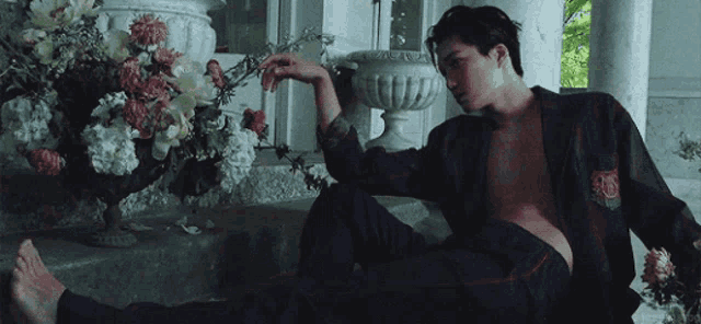a man without a shirt is laying on a porch next to a vase of flowers