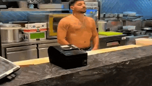 a shirtless man is standing in a kitchen behind a counter .