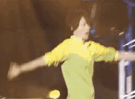 a man in a yellow shirt is dancing with his arms outstretched on a stage .