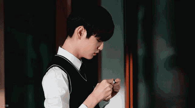 a young man wearing a white shirt and black vest is standing in front of a door