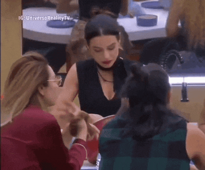 a group of women are sitting at a table holding hands and talking .