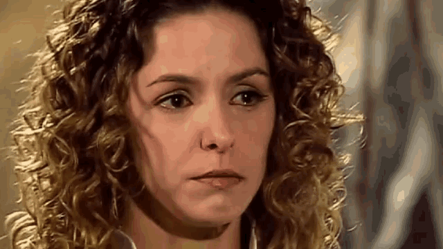 a close up of a woman 's face with curly hair making a sad face .
