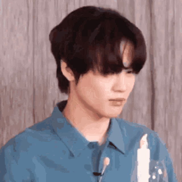 a young man in a blue shirt is sitting in front of a wooden wall holding a candle .