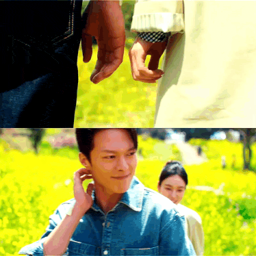 a man in a denim shirt holds a woman 's hand in a field of yellow flowers