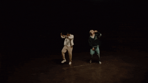 two people are dancing in a dark room and one is wearing a green jacket